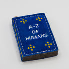 dog toy the shape of ablue book with 'A-Z of Humans' text 